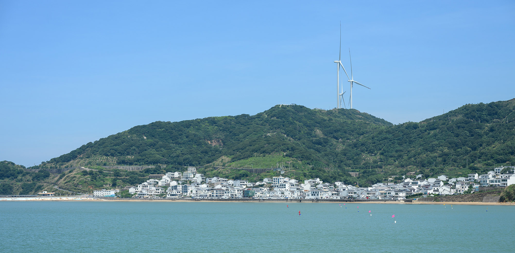 对岸视角下的衢山岛，山坡上的白色房子与山顶风车